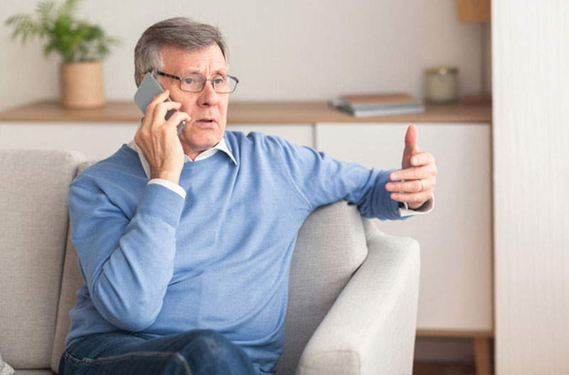 An older man speaks on the phone and knows AI scams can be used for voice cloning and number spoofing.